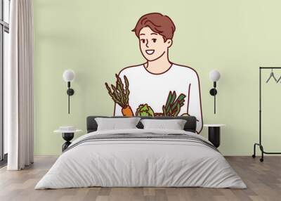 Man with basket of vegetables smiles and recommends going vegan or eating organic raw food. Vegetarian guy offers to buy farm vegetables and start new healthy diet to improve health Wall mural