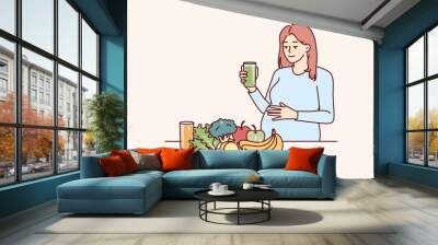 Pregnant woman drinks juice from fresh fruits and vegetables standing near steel with healthy food with vitamins. Pregnant girl is preparing to become mother and take care of unborn child Wall mural