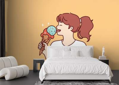 School-age girl licks large ice cream in waffle cone with fruit or caramel icing. Happy teenage girl eating ice cream enjoying summer dessert that helps to escape heat and refresh  Wall mural