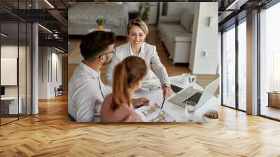 Above view of real estate agent and a couple examining blueprints during a meeting. Wall mural