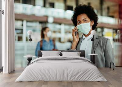 african american businesswoman wearing protective mask while making a phone call at the airport. Wall mural