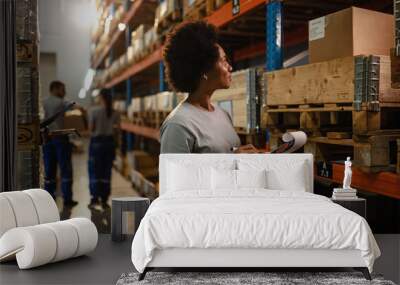 African American worker taking notes while checking stock in a warehouse. Wall mural