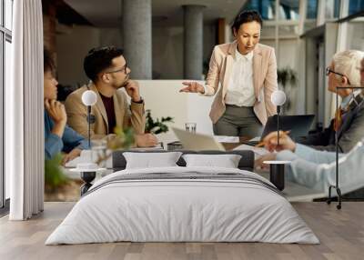 Asian female leader using laptop and communicating with her business team during meeting in the office. Wall mural