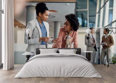 Black business mentor gives instruction to her younger colleague who works on laptop at corporate office. Wall mural