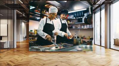 Black chef and her male coworker preparing food while working in a restaurant. Wall mural