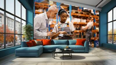 Black distribution warehouse worker and her manager using laptop at storage compartment. Wall mural