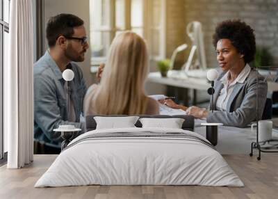 Black female insurance agent communicating with a couple during a meeting in the office. Wall mural