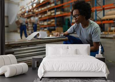 Black female worker checking list of products in a warehouse. Wall mural