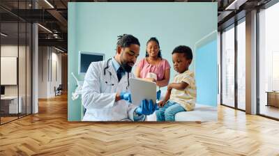 Black kid and his pediatrician using digital tablet at doctor's office. Wall mural