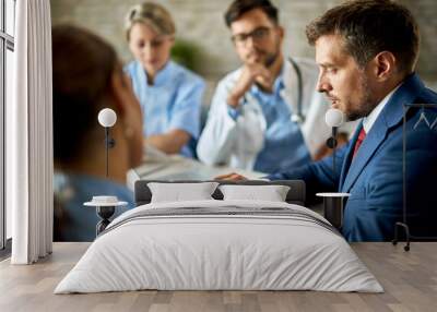 Businessman cooperating with doctors while going through reports on a meeting. Wall mural