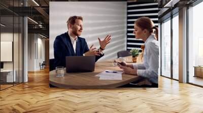 Businessman talking to female coworker while using laptop during a  meeting in the office. Wall mural