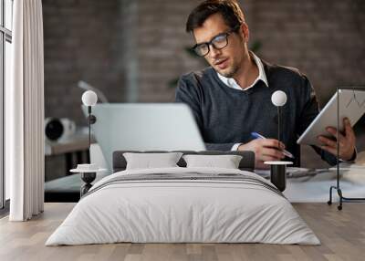 Businessman using wireless technology while working on reports in the office. Wall mural