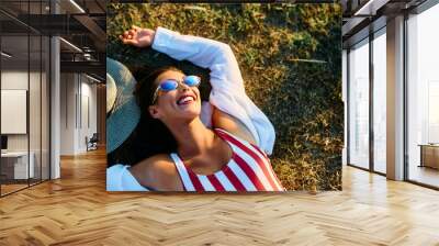 Carefree woman lying down on grass while enjoying in summer day outdoors. Wall mural