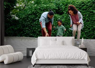 Cheerful black kid and his parents playing with soccer ball in backyard. Wall mural