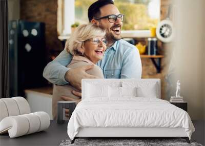 Cheerful man and his mature mother embracing in the kitchen. Wall mural