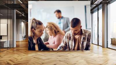 College student takes notes while studying with his female friend who is using touchpad in classroom. Wall mural