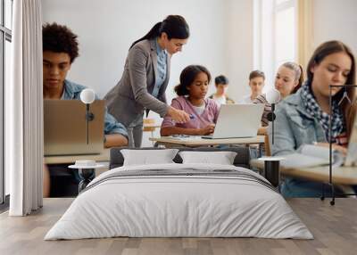 Computer science teacher assists her student in using laptop during class at high school. Wall mural