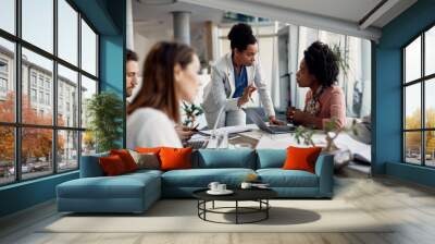 Female business mentor talks to assistant manager who works on laptop during meeting in the office. Wall mural