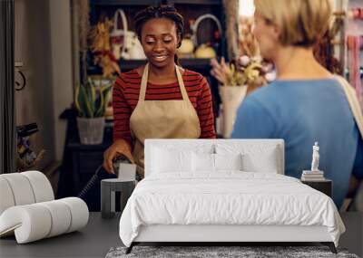 Happy African American florist receives credit card payment from her customer at flower shop. Wall mural