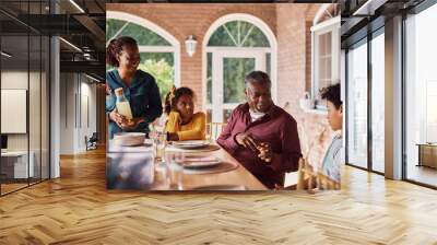 Happy African American kids and their grandparents talk at dining table on patio. Wall mural