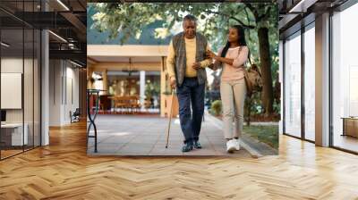 Happy African American woman walks with her senior father while visiting him at nursing home. Wall mural