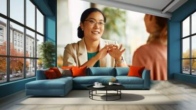 Happy Asian entrepreneur talks to her colleague during coffee break in cafe. Wall mural