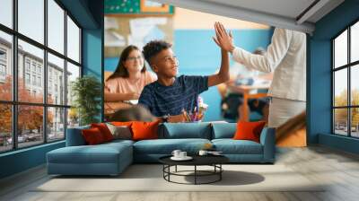 Happy black elementary student and his teacher greet with high five gesture during class at school. Wall mural