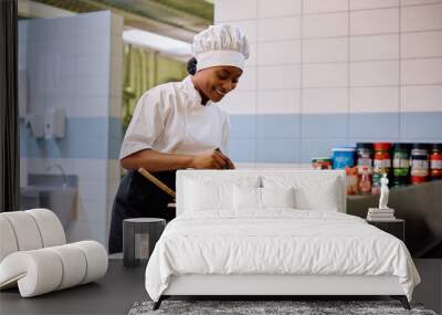 Happy black female chef cooking in kitchen in restaurant. Wall mural