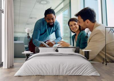 Happy black financial advisor using touchpad with his clients during meeting in office. Wall mural