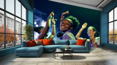 Happy black woman dancing while attending summer music festival at night and looking at camera. Wall mural