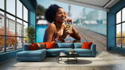 Happy black woman drinks cocktail at pool on summer vacation. Wall mural