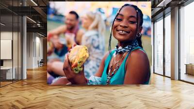 Happy black woman eating burger during open air music festival and looking at camera. Wall mural