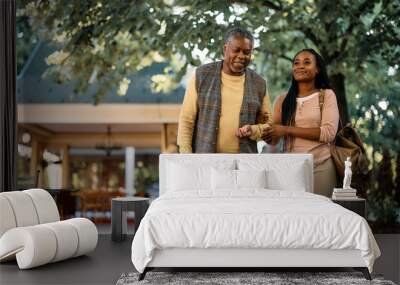 Happy black woman walks with her senior father while visiting him at nursing home. Wall mural