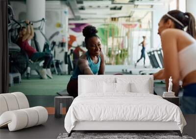 Happy black woman warming up with her female friend during sports training in gym. Wall mural