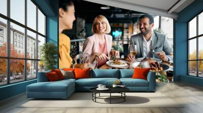 Happy business colleagues talk while eating lunch in restaurant. Wall mural