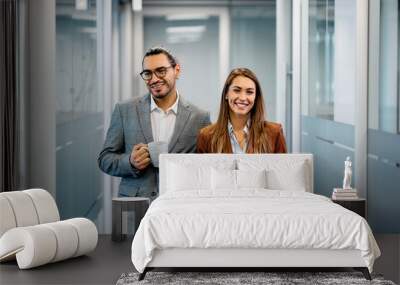 Happy businesswoman and her Hispanic male colleague in hallway looking at camera. Wall mural