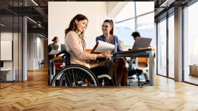 happy businesswoman in wheelchair going through reports while working female coworker in the office. Wall mural