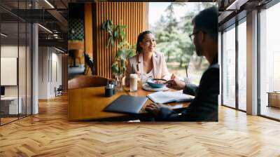 Happy businesswoman talks to colleague while eating breakfast in cafe. Wall mural