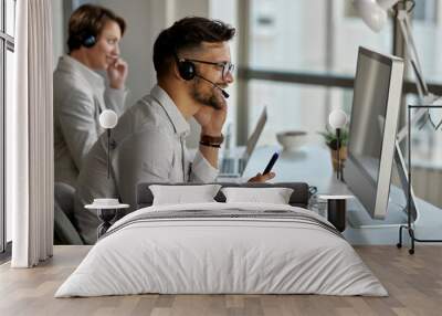 Happy call center agent using computer while communicating with clients  in the office. Wall mural