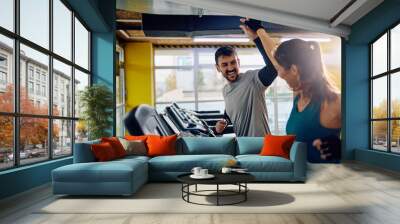 Happy couple giving high five while exercising on treadmill in gym. Wall mural