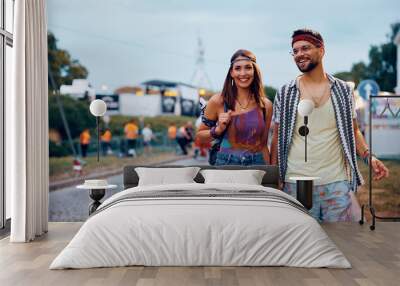 Happy couple of festivalgoers holding hands while going on open air concert. Wall mural