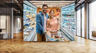 Happy couple shopping in supermarket and looking at camera. Wall mural