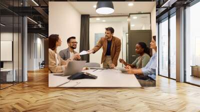 Happy entrepreneur passing business reports to his coworkers during  meeting in office. Wall mural