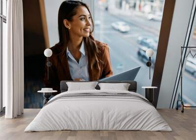 Happy female entrepreneur using laptop and looking through window in office. Wall mural