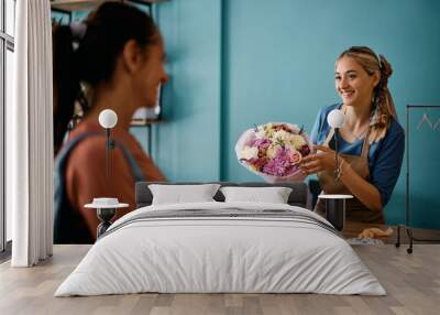 Happy florist talks to customer while selling her bouquet of flowers at floral store. Wall mural