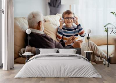 Happy kid listening music over headphones while spending time with grandfather at home. Wall mural