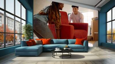 Happy man and his African American girlfriend carrying armchair while relocating into new home. Wall mural