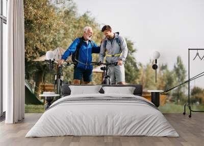 Happy man and his senior father talk while preparing for bicycle riding in nature. Wall mural