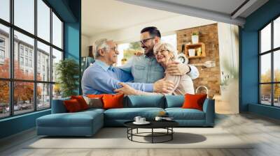 Happy man embracing his senior parents while visiting them at home. Wall mural