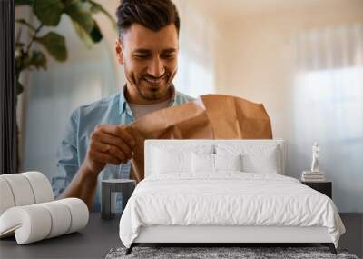 Happy man looking at food in delivery paper bag at home. Wall mural